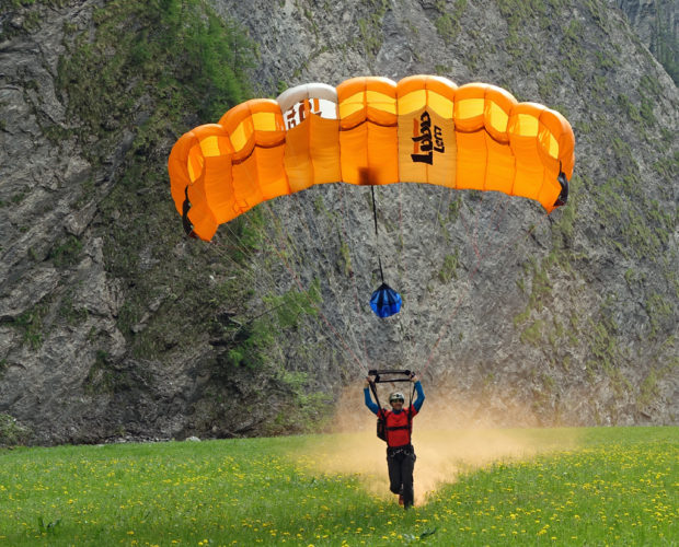 Parachutist landing with orange canopy in meadow