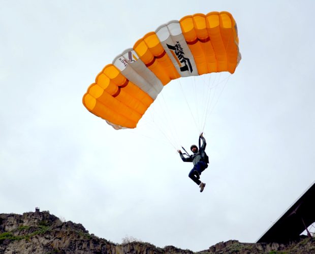 Skydiver descending under orange parachute above cliffs