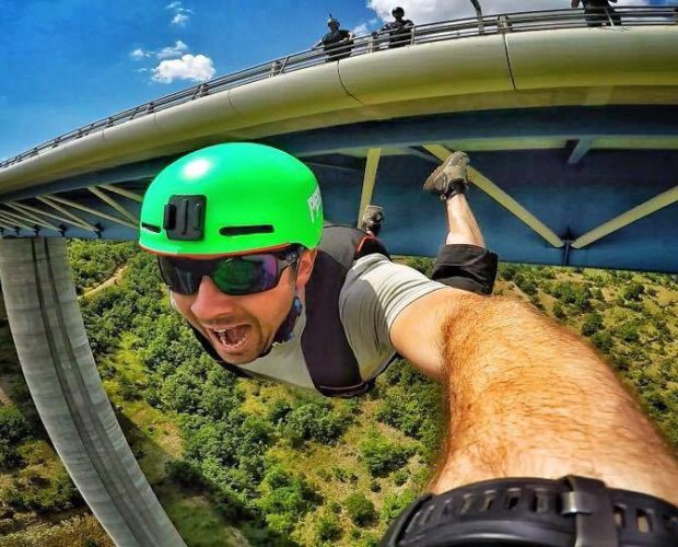 Man hanging under bridge taking selfie